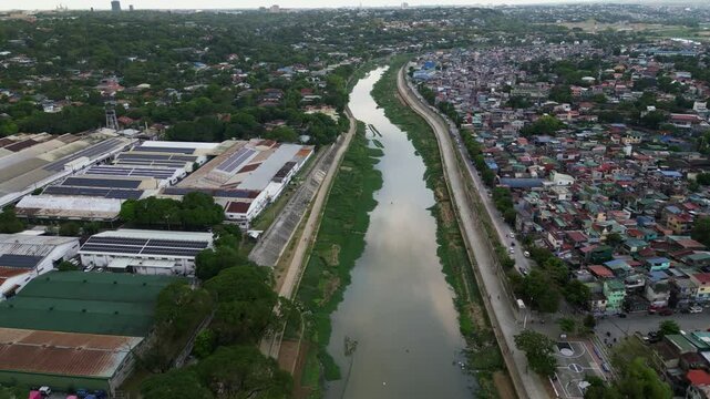 Marikina River flows through urban corridor flanked by rooftops and narrow parallel roads, aerial tracking dolly
