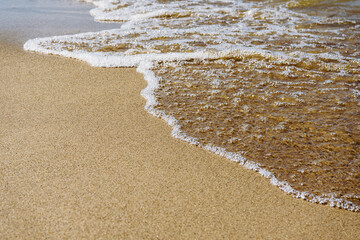 Wave on brown sand, close-up. Summer beach background