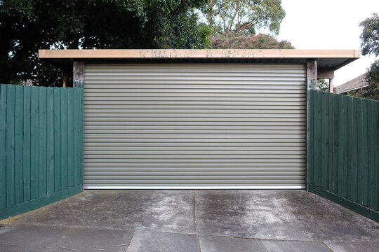 A garage roller door in between green fences