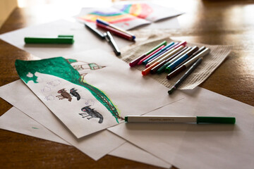 Child's drawing of sheep, dogs and a farm sitting on a table with textas and other art materials