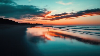 Fototapeta premium Stunning sunset over calm sea with reflections on sand, a peaceful beach scene in vibrant colors and a person standing on shore.