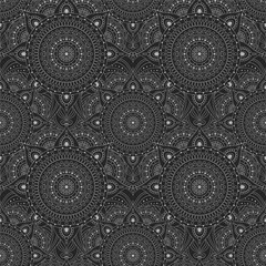 Dark abstract seamless pattern with white ethnic ornaments on a black background. Oriental and Asian-inspired designs with circular patterns or mandalas.