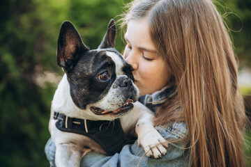 12 year old girl kissing and hugging french bulldog in park.