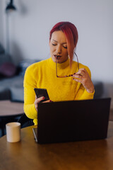 Focused freelancer working remotely from home office using laptop and smartphone