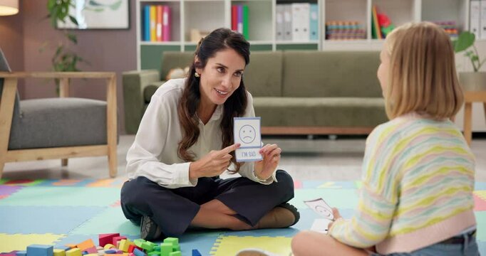 Psychologist, emotion test and child in therapy for learning, talk or help for development. Kid, woman and counseling session in office with card for feelings, cognitive behavior and cbt for sad mood