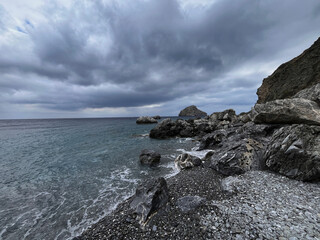 Wild rocky coastline with stormy clouds over Aegean Sea on Amorgos Island, Greece – dramatic...