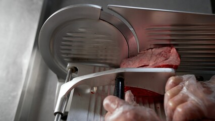 Butcher slicing red meat with professional slicer in butchery