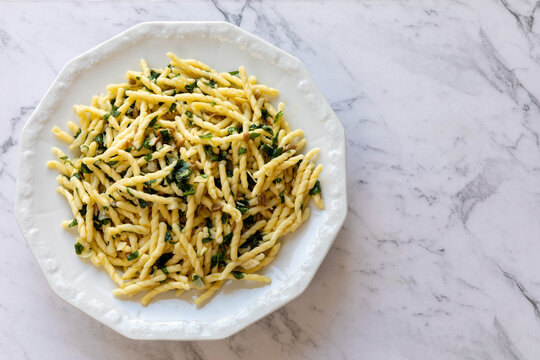 Trofie pasta with roughly chopped pesto on a plate. Trofie al Pesto - famous Ligurian dish. Marble background with copy space. 