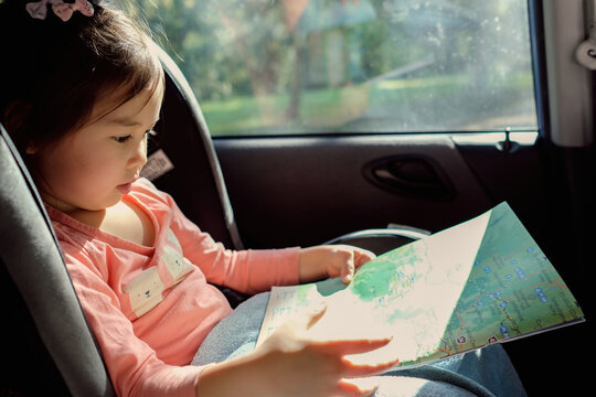 Young girl in car seat reading map on road trip