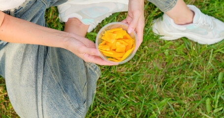 Close-up of a girl picking dried mango from a container in the park.