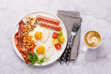 A classic breakfast plate featuring sunny-side-up eggs, crispy bacon, sausages, and fresh tomatoes