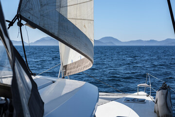 Obraz premium open sails, view of catamaran white deck in open blue sea, mountain horizon