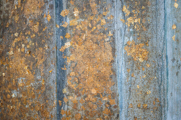 A close-up of an ancient Buddha statues surface with scattered gold leaf patches applied across the aged texture.