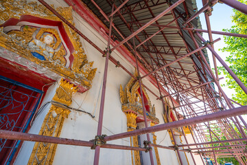 A temple under restoration at Sai Areerak Temple, Ratchaburi, Thailand, with scaffolding over ornate golden frames and intricate carvings.