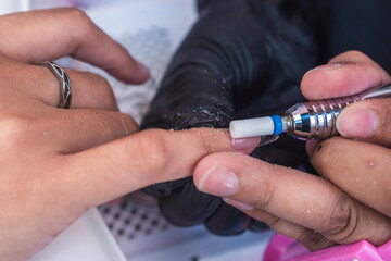 Close-up of a beauty technician using a ceramic barrel bit on an electric drill to seamlessly blend a soft gel tip with the natural nail surface.