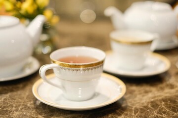 Close-up of a fine bone china teacup with gold trim and a pot of Taiwanese tie guan yin oolong tea at the lounge of Montien Surawong, a hotel in Silom - Bang Rak, Bangkok, Thailand