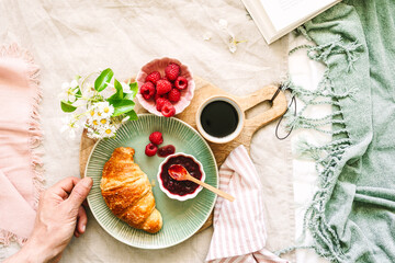 Süsses Frühstück im Bett mit knusprigen Croissant, frischen Himbeeren und einer Tasse Kaffee. Draufsicht.