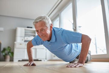 Senior man doing push-ups indoors with a smile