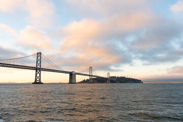 Bay Bridge stretching across the horizon beneath a soft sunset sky viewed from the San Francisco ferry on May 11, 2019