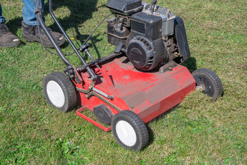Gardener works with a scarifier, removing moss and thatch from a lawn, improving its health and appearance seasonal Gardening on a bright sunny spring day,