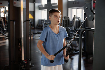 Teenage boy training press at rowing machine at modern fitness center