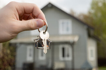 Man hand holds house-shaped key in front of newly purchased home. New beginning, homeownership, and...