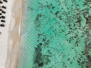 Top-down view of white sand beach, umbrellas and shallow reef-filled turquoise waters in Le Morne