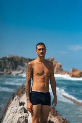 Chico joven tatuado en la playa de rocas, Playa de la Arnía, Santander, España