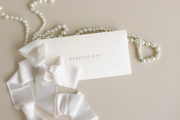 Wedding invitation envelope, greeting card mockup with white silk ribbon and pearl necklace on beige background top view.Copy space. Wedding backdrop. © irenastar