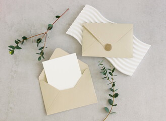 Beige envelope with blank paper card mockup  inside top view decor and eucalyptus leaves on beige textured background. Copy space.Wedding invitation mockup, greeting card, holiday concept.