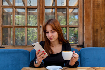 Young woman drinking coffee and reading phone at outdoor caf