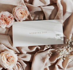 Wedding invitation envelope, greeting card mockup with roses flowers frame on beige silk background top view.Copy space. Wedding , birthday, holiday backdrop.