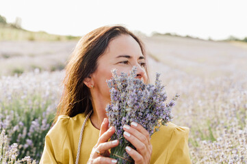 woman in yellow dress stands in lavender field, gently holding bouquet of lavender flowers. She appears serene and contemplative, enjoying beauty and fragrance of blossoms around her.