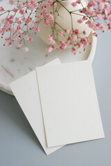 Greetings card blank mockup and pink flowers in a vase on light blue background with copy space.Top view. Empty blank, card mock up, template, Mother's day backdrop, birthday, holiday.
