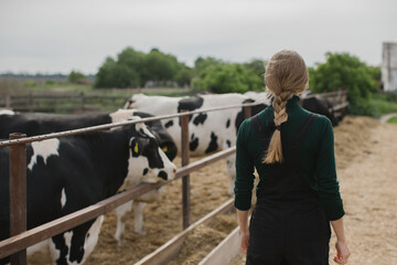 Young female farm worker near a paddock with cows outdoors.