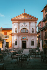 Fototapeta premium Front view of a church in the historic center of Intra, Verbania, surrounded by typical Italian buildings and outdoor café seating in a cozy piazza