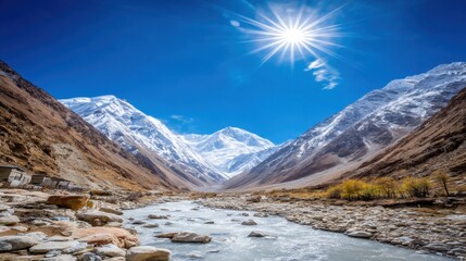 Snow-capped mountain range with glacial river and rocky valley under bright sun and clear blue sky
