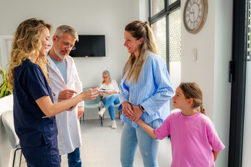 Doctor and nurse are discussing a medical chart with a mother and her daughter in the waiting room...