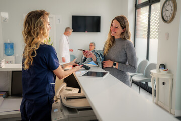 Pregnant woman is completing a contactless payment transaction at the reception desk of a modern...