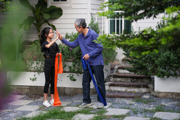 Young asian kindergarten girl is doing exercise with her grandfather in the backyard garden for healthy and sport