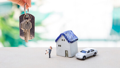 House key in girl hand with happy couple and house model with model car over blurred swimming pool...