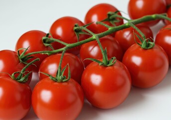 Close-up of a vibrant bunch of ripe red cherry tomatoes still attached to their green stem on a white surface