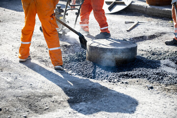 Construction workers repairing a road with asphalt material on a sunny day in an urban setting
