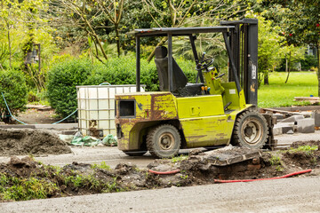 Rusty yellow forklift parked at urban construction site with tools, pipes and earth piles around...