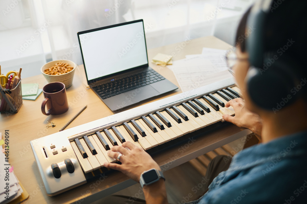 Poster man playing electronic keyboard at workstation with laptop and assorted office supplies around creat