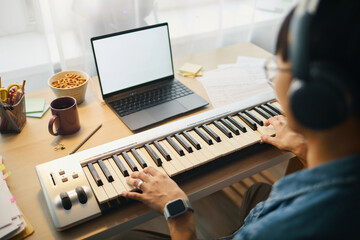 Man playing electronic keyboard at workstation with laptop and assorted office supplies around...