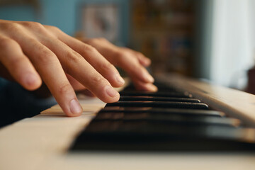 Close-up shot of hands playing on piano keys in a softly lit room, creating a warm and serene...
