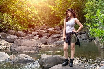 Young Asian Woman Standing on Rocky Riverbank in Forest During Outdoor Adventure