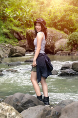 Young Asian Woman Standing on Rocky Riverbank in Forest During Outdoor Adventure