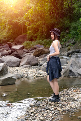 Young Asian Woman Standing on Rocky Riverbank in Forest During Outdoor Adventure